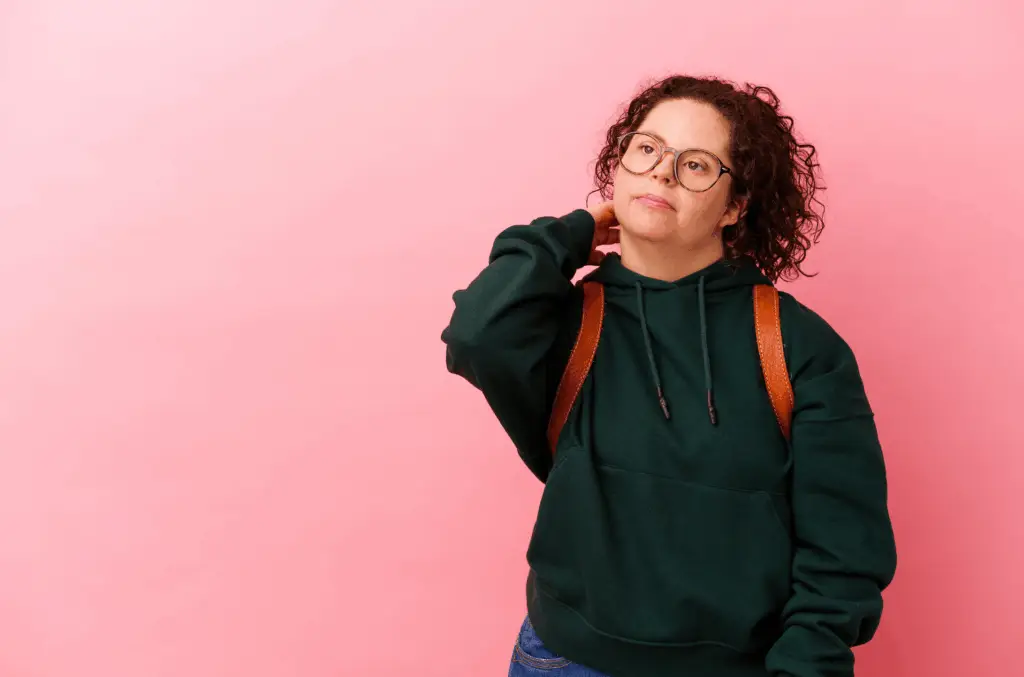 Young woman with a backpack looking thoughtfully to the side against a pink background